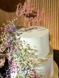 Close up bruidstaart van Zoete Kruimels met roze acryl taarttopper 'better together' en gekleurd gipskruid