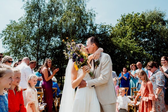 Bruidspaar die elkaar omhelst en kust bij ceremonie met de gasten op de achtergrond