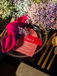 CLose up diner bord met gouden rand, roze acryl menu , roze acryl naamkaartje, roze servet, gipskruidtakje en gouden bestek
