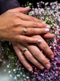 Close up handen bruidspaar met trouwringen boven boeket van gekleurd gipskruid