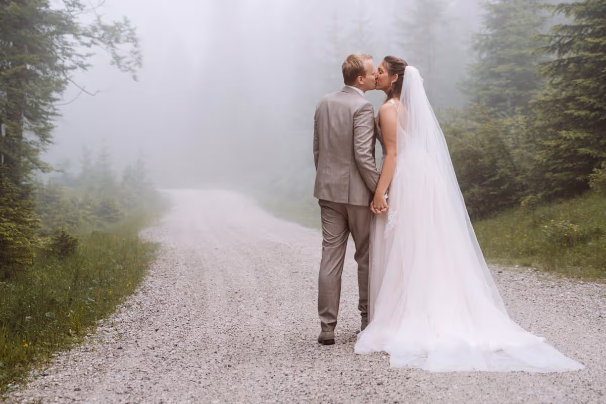 Kussend bruidspaar op bospad met mist op de achtergrond