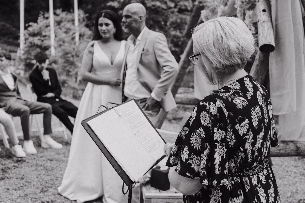 zwart wit foto van het zijaanzicht vsn trouwambtenaar karin waar ze achter haar katheder staat p de achtergrnd staat het bruidspaar